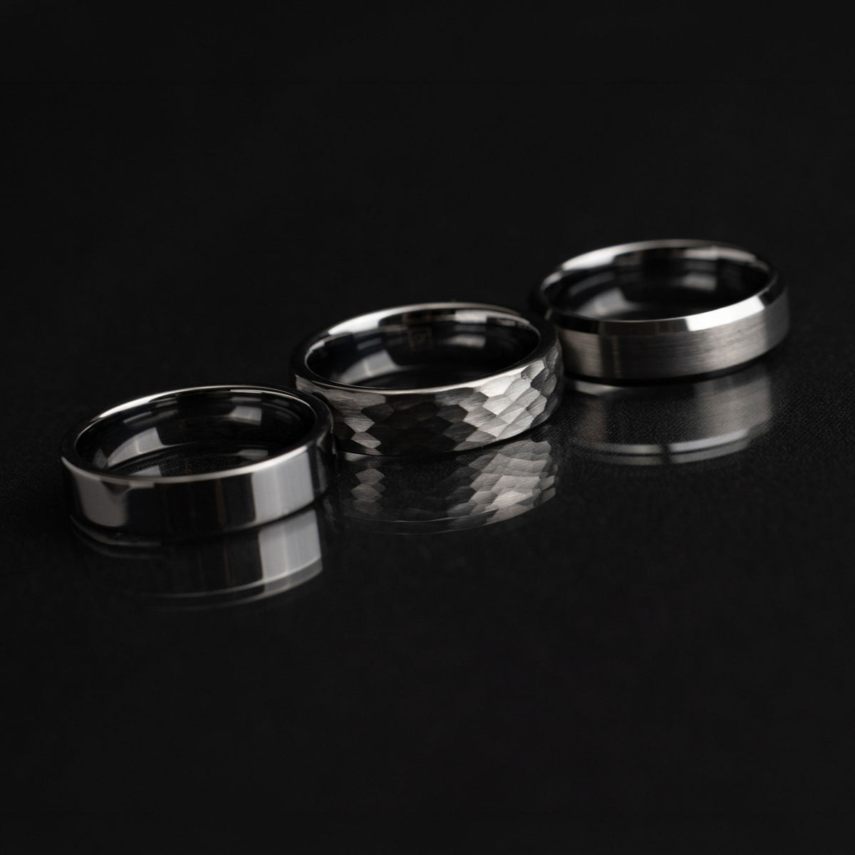 A close-up of Project Atomic tungsten rings showing their substantial profiles and natural, black and gold-plated finishes.